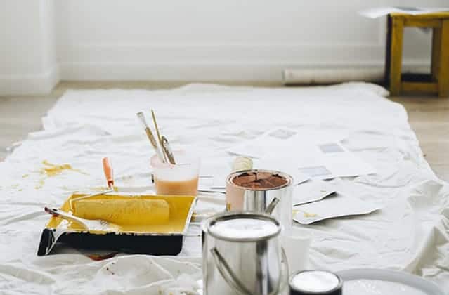 white sheet on floor with paint tins, paint roller and tray and samples