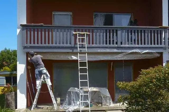 front of home with man painting double story deck